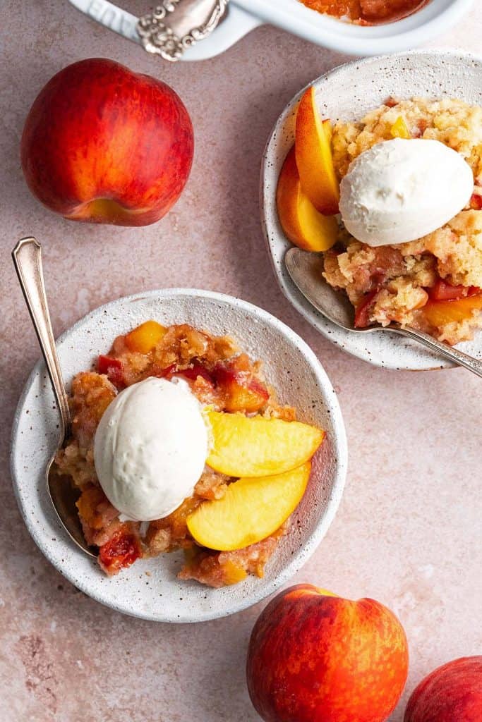 top view of warm peach dump cake in bowls with ice cream and fresh peaches